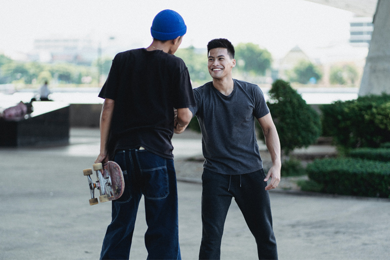 Zwei junge Männer begrüßen sich, einer hält ein Skateboard in der Hand